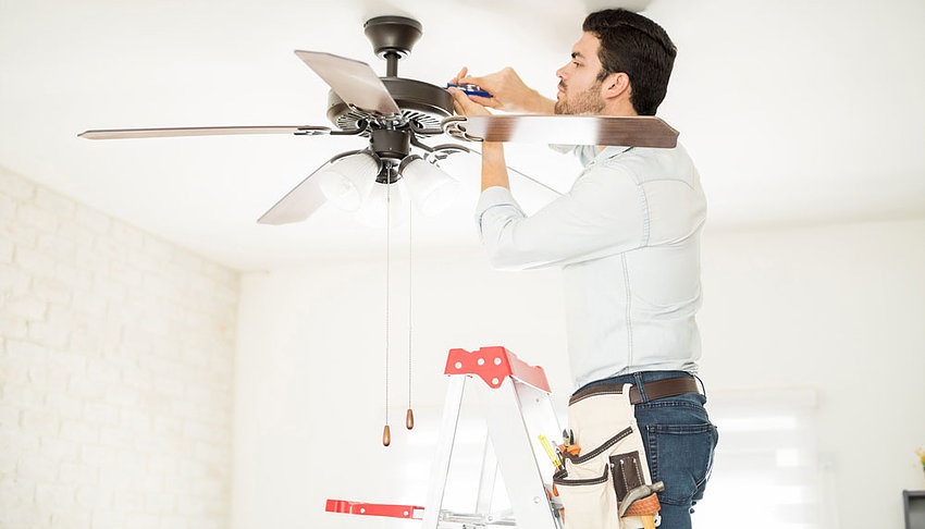 Our electrician fixing a fan in a living room while standing on a ladder